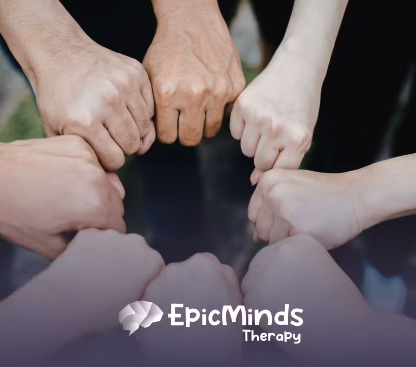 Seven hands form a circle with fists touching in the center, symbolizing unity and teamwork.