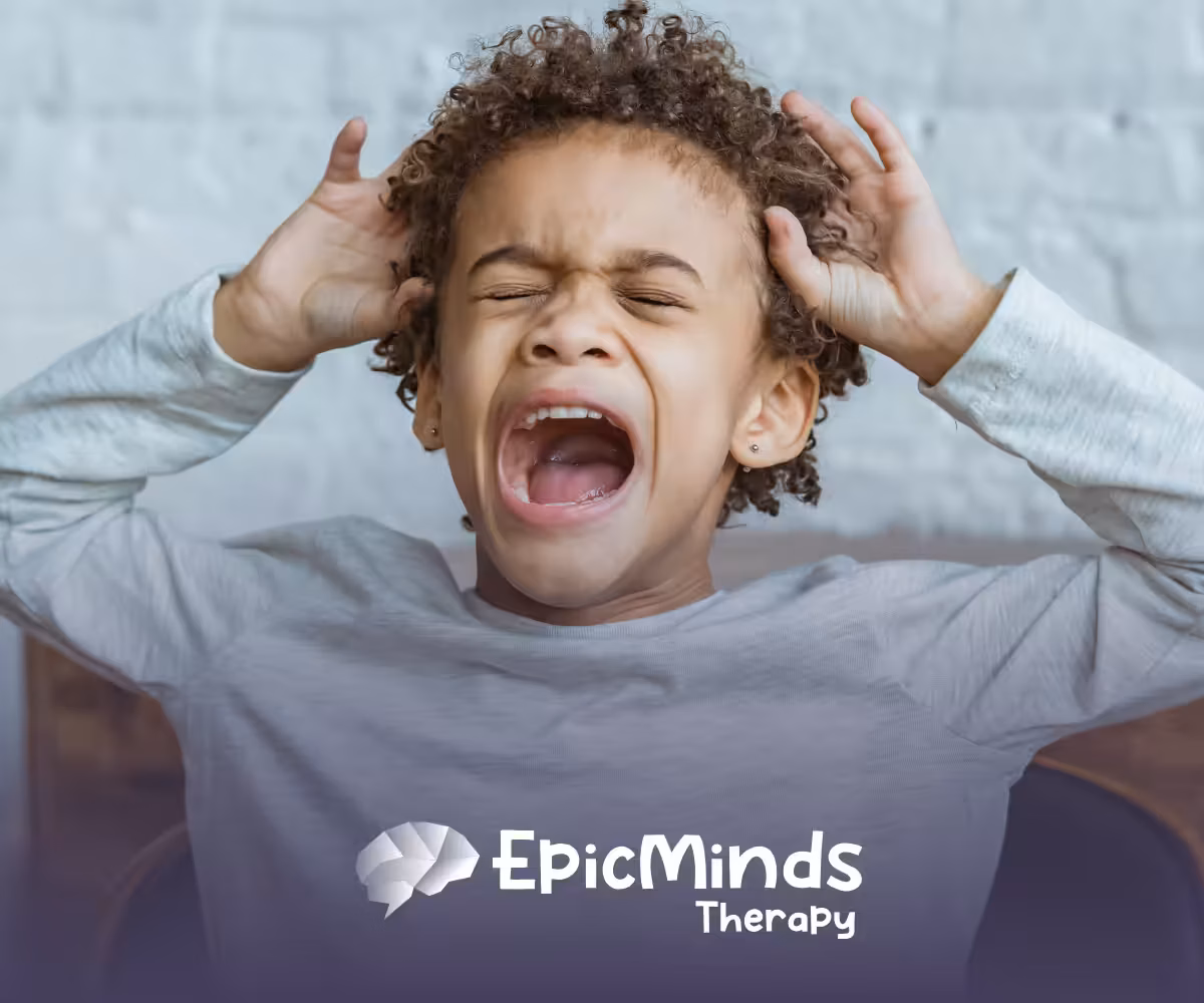 Young child with curly hair screaming with eyes closed and hands gripping their head against a white brick wall