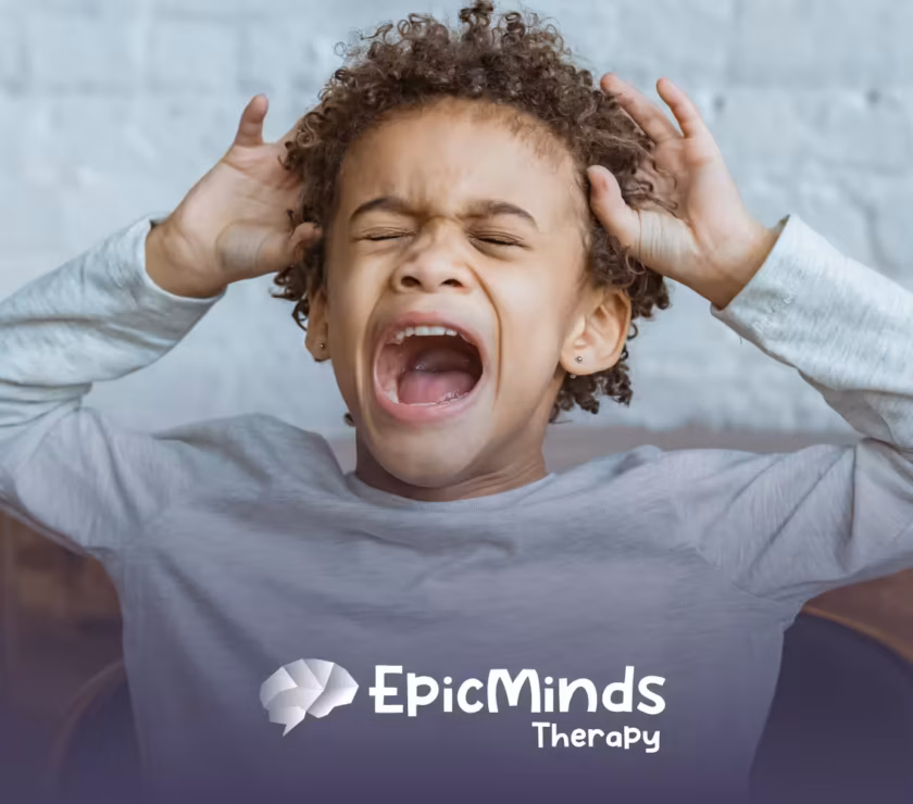 Young child with curly hair screaming with eyes closed and hands gripping their head against a white brick wall