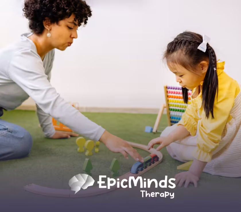 Woman and young girl playing together with a wooden train set on a green play mat in a bright room
