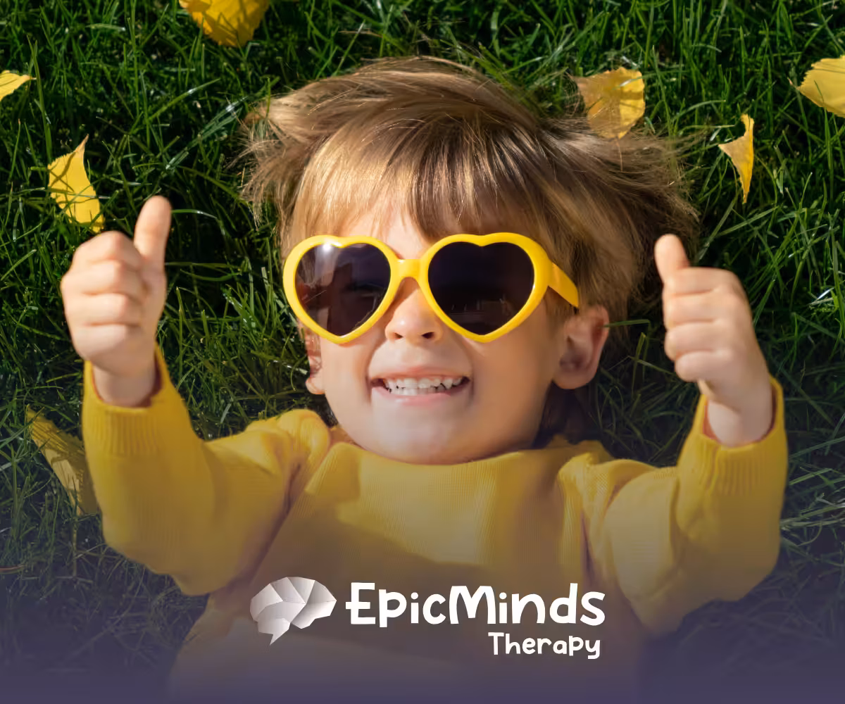 A smiling kid lying on the grass and facing the sky with sunglasses on