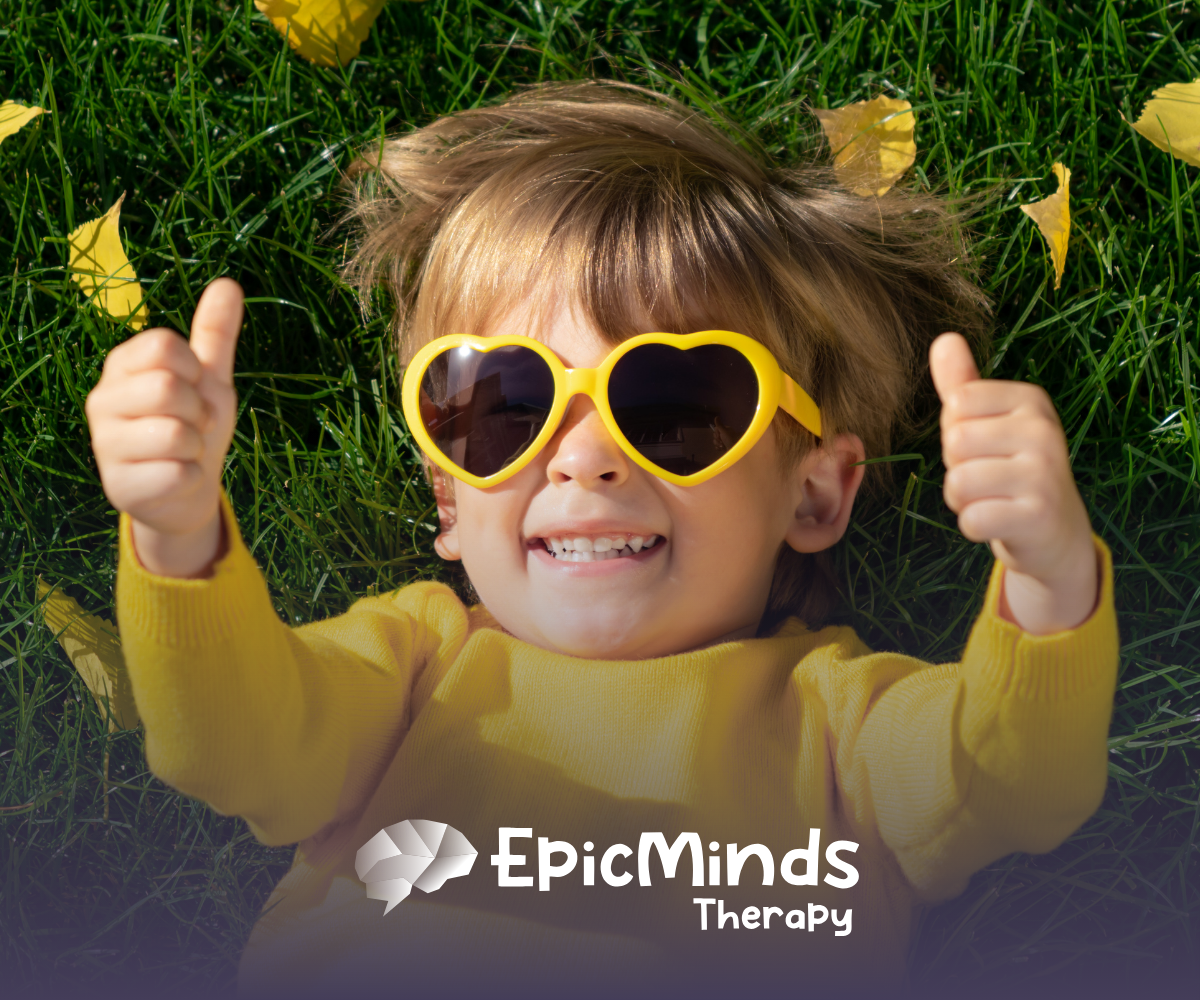 A smiling kid lying on the grass and facing the sky with sunglasses on