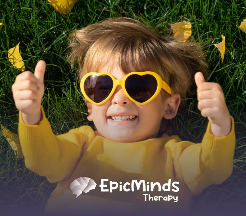 A smiling kid lying on the grass and facing the sky with sunglasses on