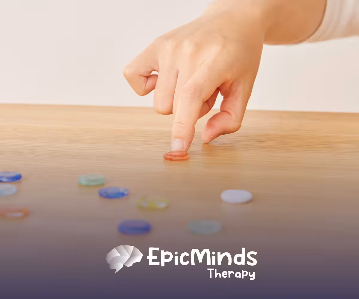 Hand pressing a small red glass token onto a wooden table surrounded by scattered colorful tokens