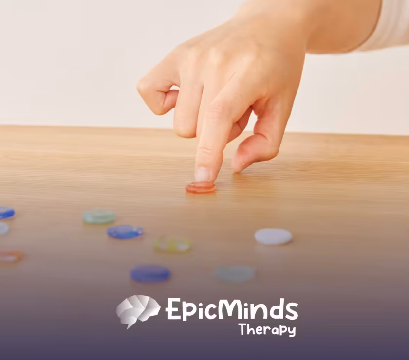 Hand pressing a small red glass token onto a wooden table surrounded by scattered colorful tokens